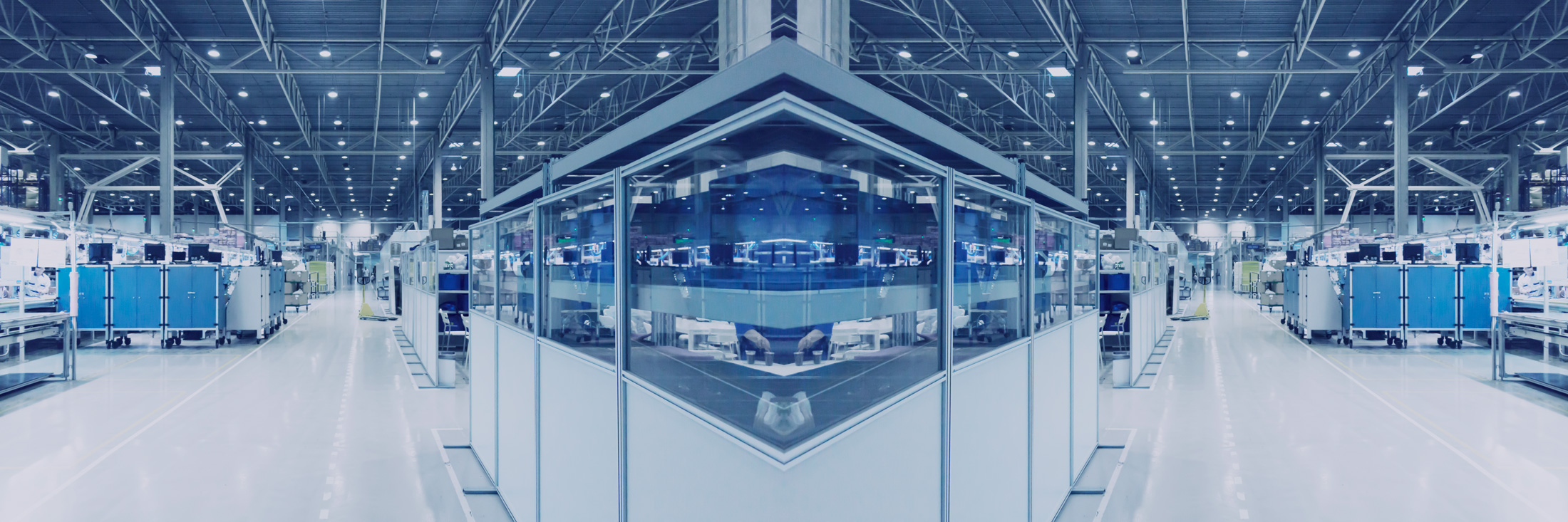 A panoramic view of a modern industrial facility with assembly lines, illuminated ceiling lights, and blue workstations along the sides of a wide aisle.